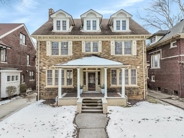 view of front of house with a chimney, a porch, and brick siding