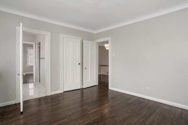 unfurnished bedroom with a closet, dark wood-style flooring, and baseboards