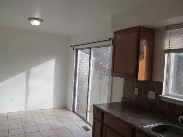 kitchen with light tile patterned floors, visible vents, dark countertops, backsplash, and a sink