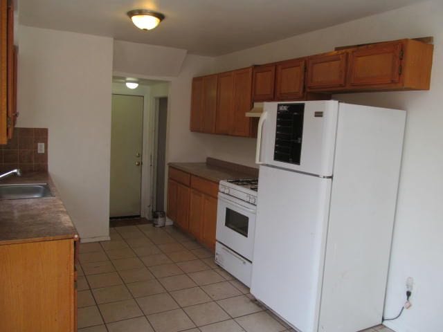 kitchen with white appliances, a sink, brown cabinets, tasteful backsplash, and dark countertops