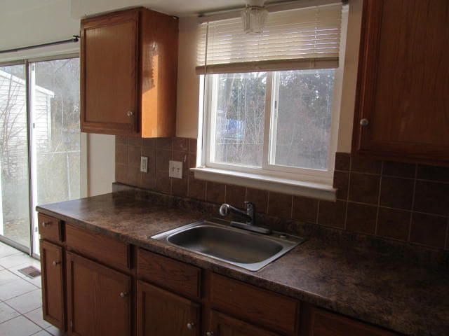 kitchen with light tile patterned floors, decorative backsplash, dark countertops, brown cabinets, and a sink