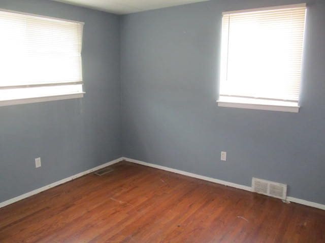 unfurnished room with dark wood-style flooring, visible vents, and baseboards