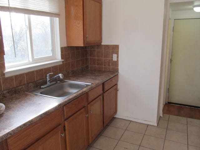 kitchen featuring backsplash, dark countertops, a sink, and brown cabinets