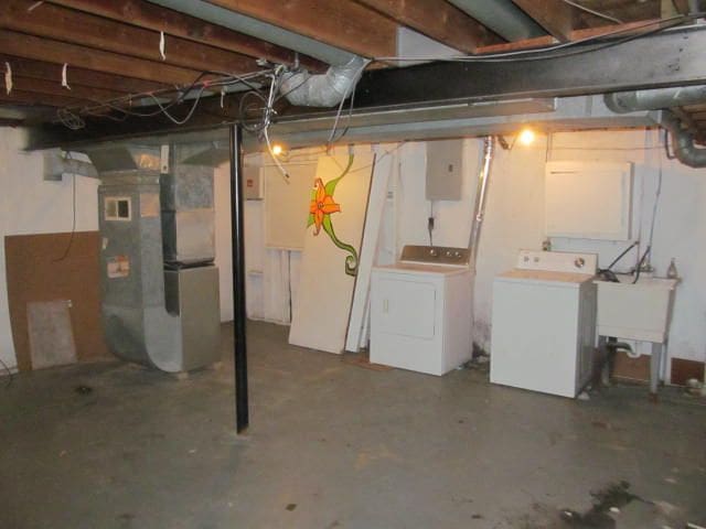 unfinished basement with a sink, washing machine and clothes dryer, electric panel, and heating unit