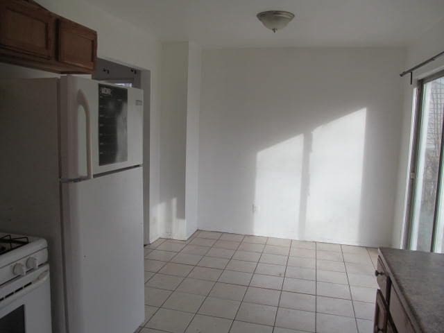 kitchen featuring light tile patterned floors, white appliances, brown cabinetry, and dark countertops