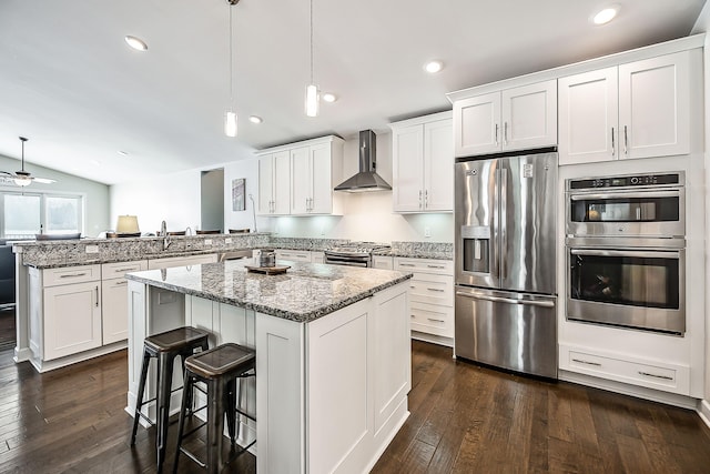 kitchen featuring wall chimney range hood, a peninsula, stainless steel appliances, and dark wood-style floors