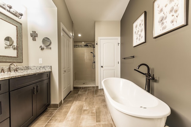 bathroom featuring a stall shower, a freestanding tub, vanity, baseboards, and recessed lighting