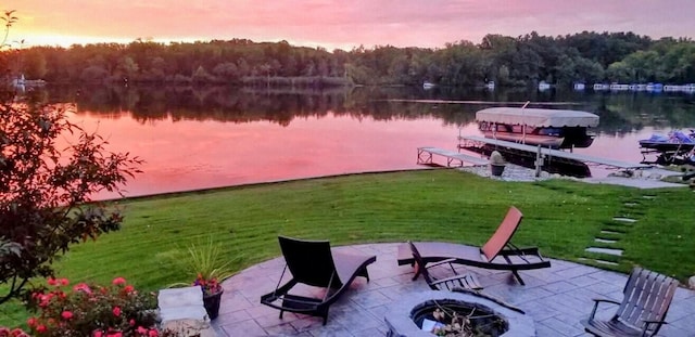 view of dock featuring a patio area, a lawn, a water view, boat lift, and a view of trees