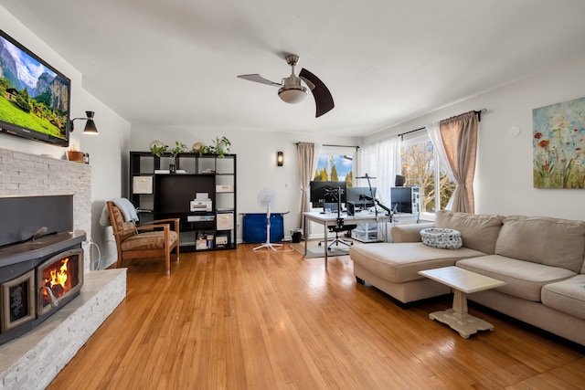 living room featuring light wood-type flooring, a fireplace, and a ceiling fan