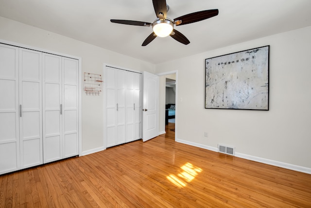 unfurnished bedroom with two closets, visible vents, ceiling fan, light wood-type flooring, and baseboards