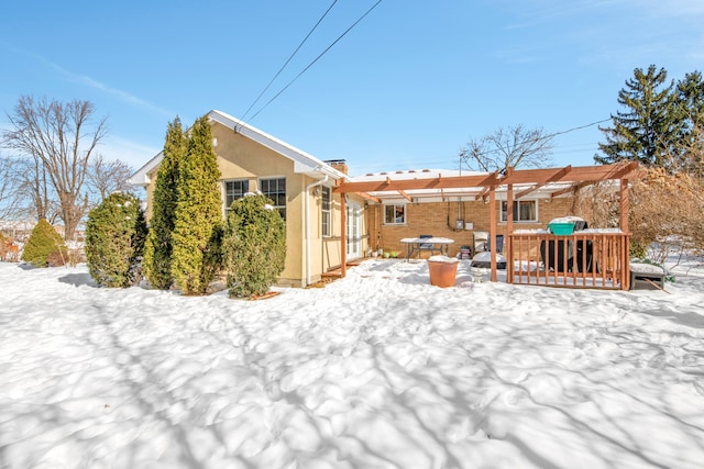 snow covered back of property with a pergola, a wooden deck, and stucco siding