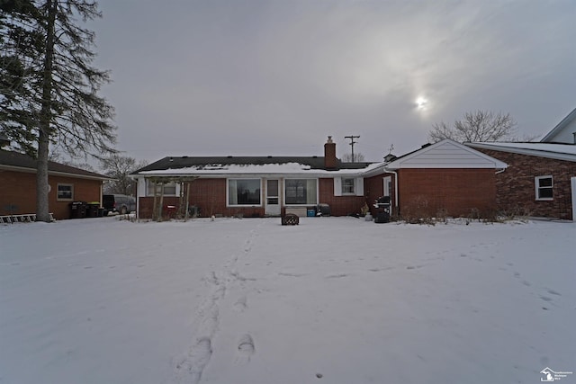 snow covered rear of property featuring a chimney and brick siding