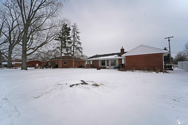 snow covered rear of property with brick siding and a chimney