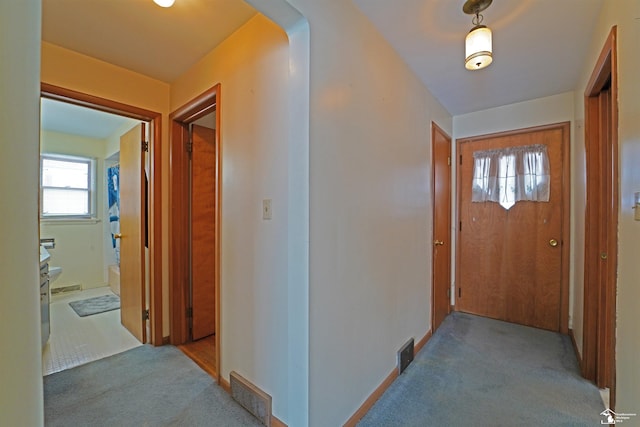 hallway featuring arched walkways, visible vents, plenty of natural light, and light carpet