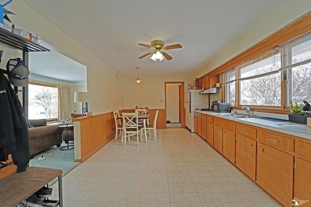 kitchen featuring ceiling fan, brown cabinets, freestanding refrigerator, light countertops, and a sink