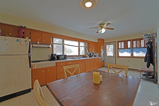 kitchen featuring freestanding refrigerator, light countertops, under cabinet range hood, black microwave, and a sink