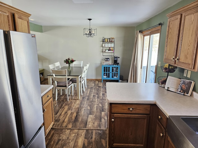 kitchen featuring light countertops, brown cabinetry, freestanding refrigerator, and pendant lighting