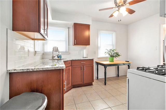 kitchen with brown cabinets, white gas stove, light tile patterned floors, backsplash, and a sink