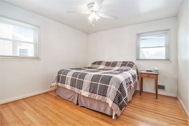 bedroom featuring baseboards, multiple windows, visible vents, and wood finished floors