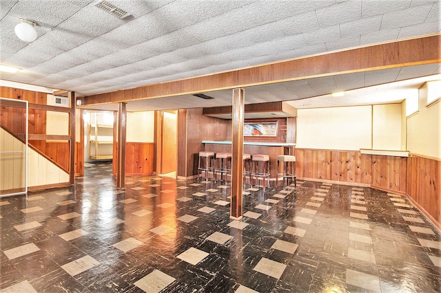 finished basement featuring a bar, wood walls, visible vents, and wainscoting