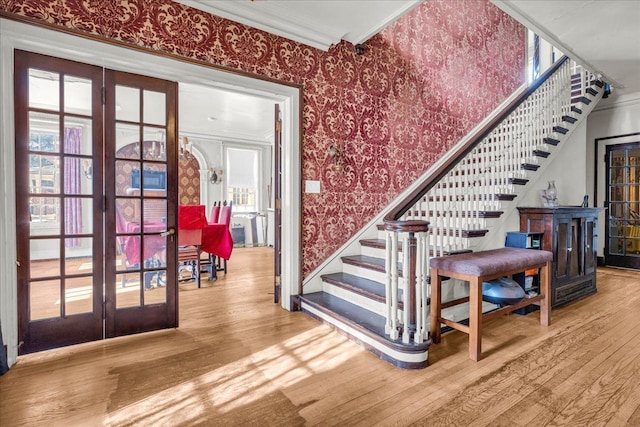 stairs with ornamental molding, wood finished floors, french doors, and wallpapered walls