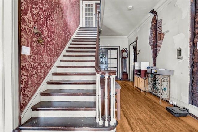 stairway with wallpapered walls, ornamental molding, and wood finished floors