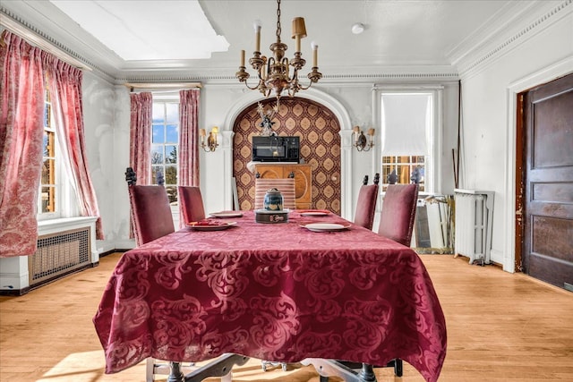 dining space with ornamental molding, radiator heating unit, light wood-style flooring, and an inviting chandelier