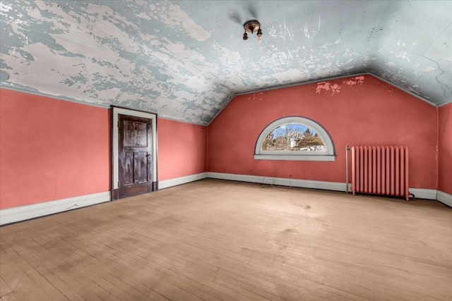 additional living space featuring radiator, light wood finished floors, baseboards, and vaulted ceiling