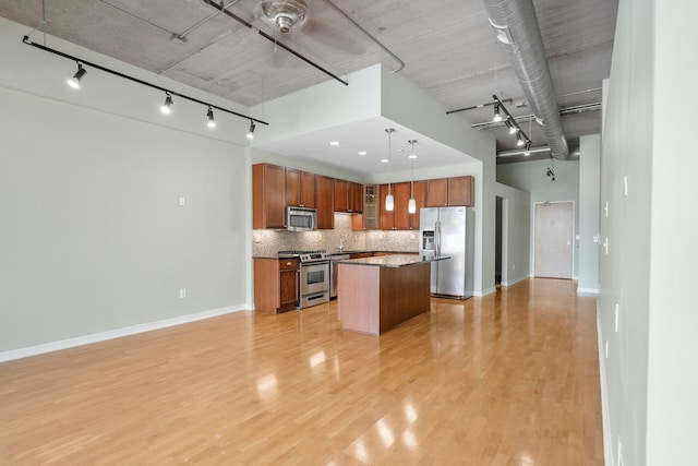 kitchen featuring stainless steel appliances, a kitchen island, light wood-style floors, open floor plan, and hanging light fixtures