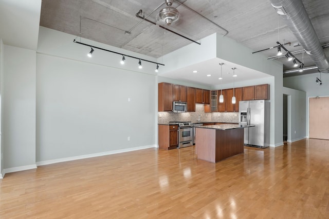 kitchen with dark countertops, open floor plan, a center island, stainless steel appliances, and pendant lighting