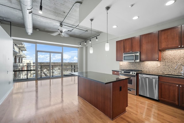 kitchen featuring decorative light fixtures, stainless steel appliances, dark countertops, a sink, and a kitchen island