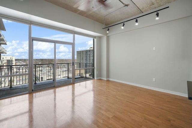 spare room featuring track lighting, a view of city, baseboards, and wood finished floors