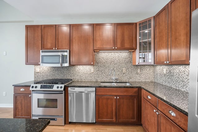 kitchen featuring a sink, appliances with stainless steel finishes, backsplash, dark stone countertops, and glass insert cabinets