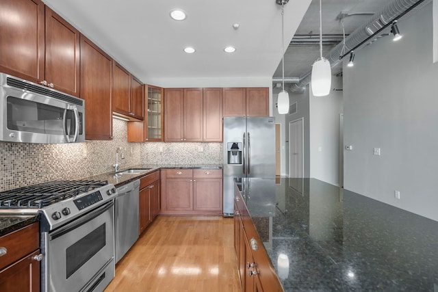 kitchen featuring stainless steel appliances, a sink, hanging light fixtures, brown cabinets, and glass insert cabinets