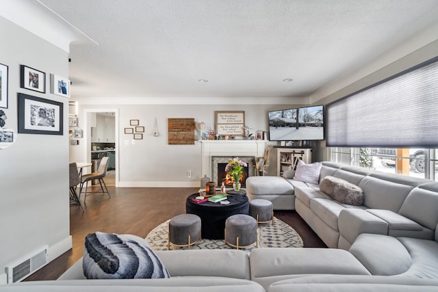 living room featuring dark wood-type flooring, visible vents, a textured ceiling, and a premium fireplace