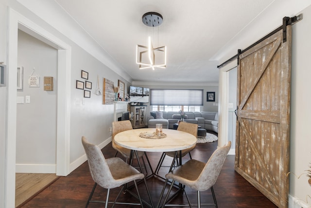 dining room with dark wood-style floors, a barn door, baseboards, and an inviting chandelier