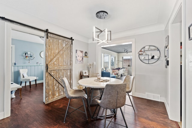 dining space featuring a barn door, dark wood finished floors, visible vents, and baseboards