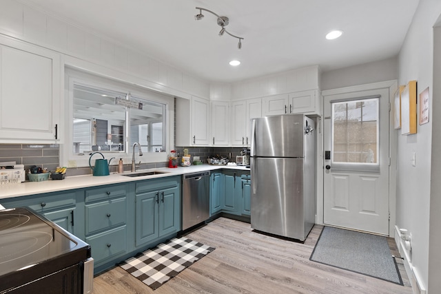 kitchen featuring appliances with stainless steel finishes, light countertops, blue cabinetry, white cabinetry, and a sink