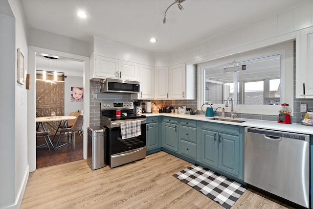 kitchen featuring light wood-style flooring, stainless steel appliances, light countertops, white cabinetry, and a sink