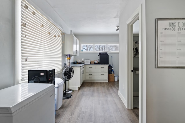 clothes washing area featuring light wood-type flooring, cabinet space, and baseboards