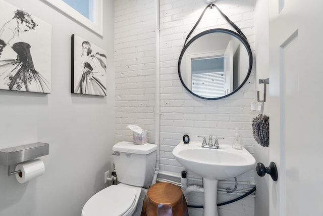 bathroom featuring brick wall, a sink, and toilet