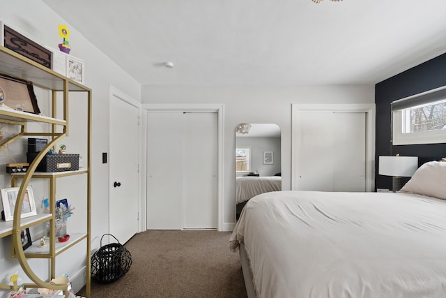 carpeted bedroom featuring arched walkways and two closets