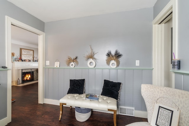 sitting room with dark wood finished floors, wainscoting, a fireplace with flush hearth, and visible vents