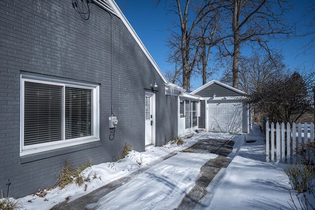 view of snow covered exterior featuring a garage, brick siding, and fence