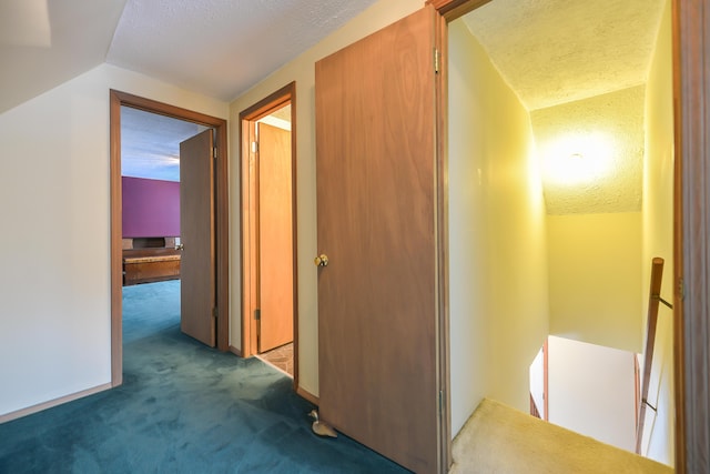 hall with dark colored carpet, vaulted ceiling, a textured ceiling, and an upstairs landing