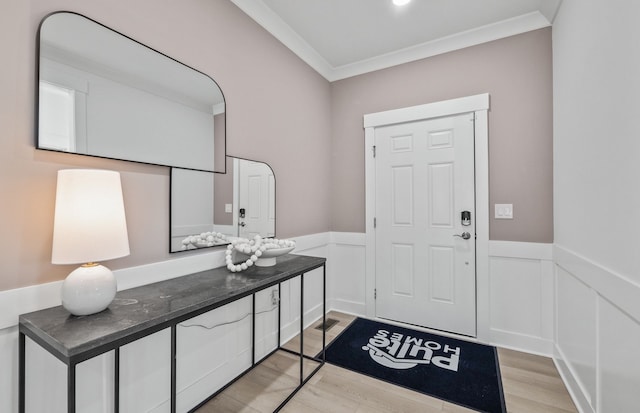 foyer entrance with a wainscoted wall, ornamental molding, and light wood finished floors