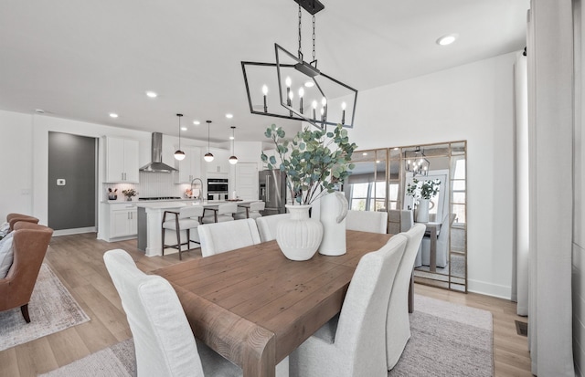 dining space with light wood-type flooring, a notable chandelier, baseboards, and recessed lighting