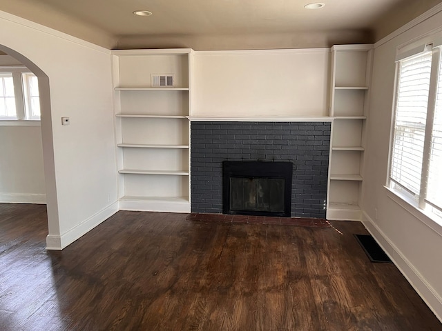 unfurnished living room featuring dark wood-type flooring, arched walkways, visible vents, and a fireplace