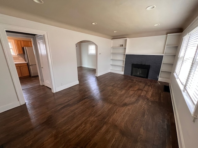 unfurnished living room with baseboards, arched walkways, dark wood-style floors, a fireplace, and recessed lighting