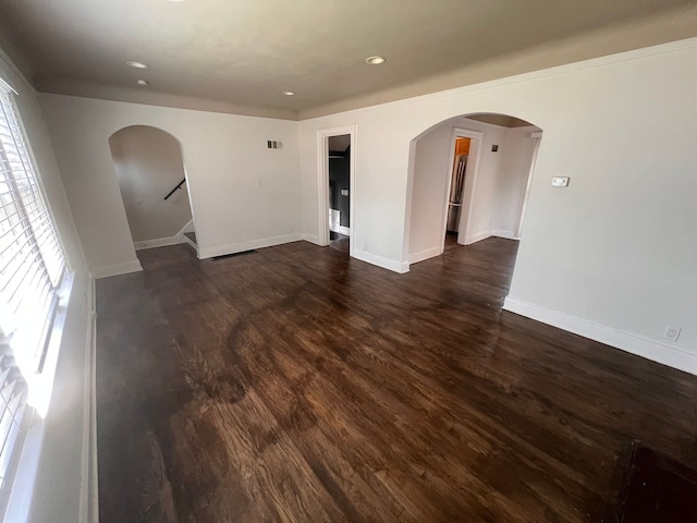 empty room featuring arched walkways, dark wood-style flooring, and plenty of natural light